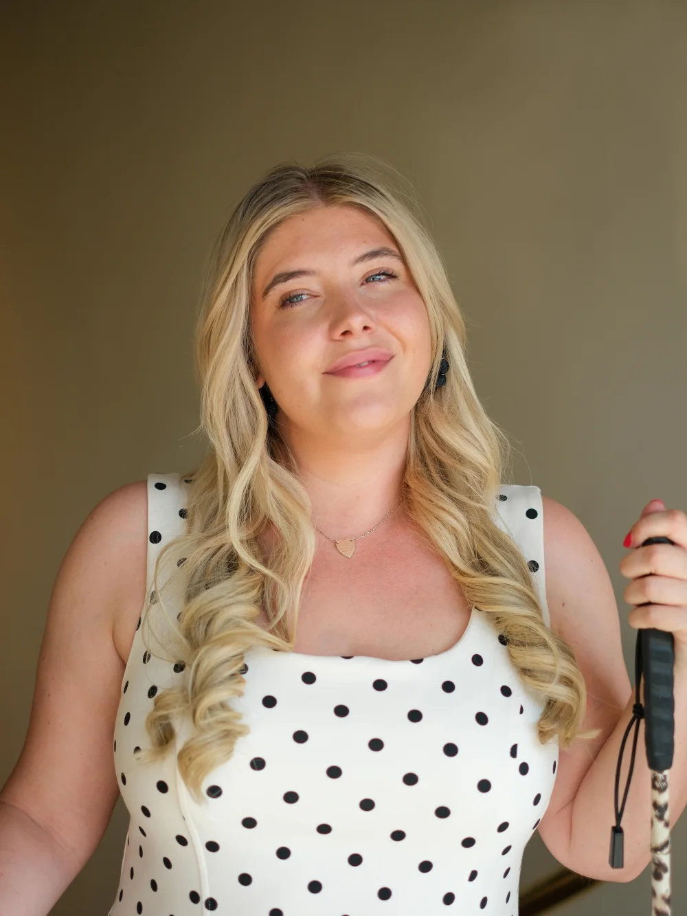 Tilly Dowler in a white polka dot dress, holding her cane, looking off to one side.