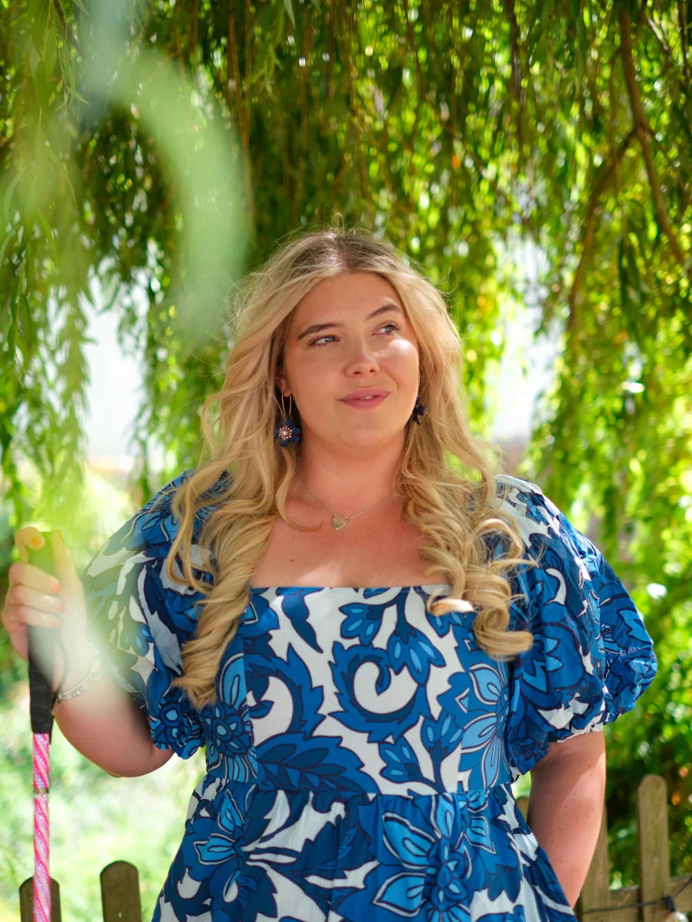 Tilly Dowler in a blue and white floral dress standing under a willow tree.